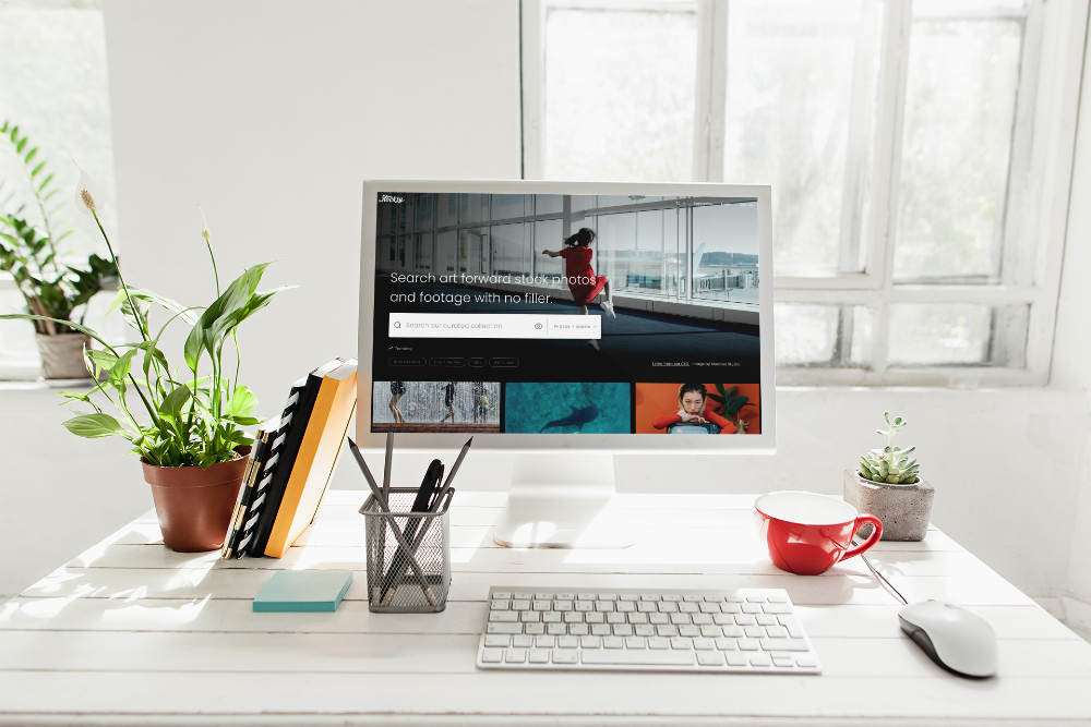 A modern desk with a computer screen showing the landing page of Stocksy stock photography site. 